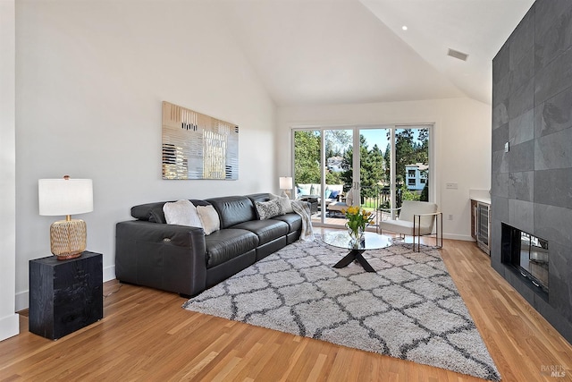 living room featuring a tiled fireplace, high vaulted ceiling, and light hardwood / wood-style flooring