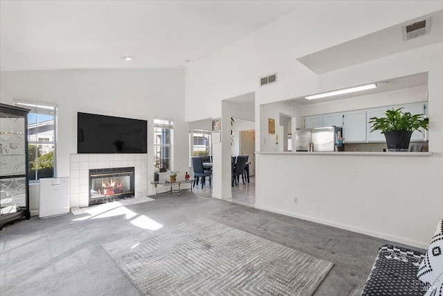 carpeted living room featuring high vaulted ceiling and a tiled fireplace