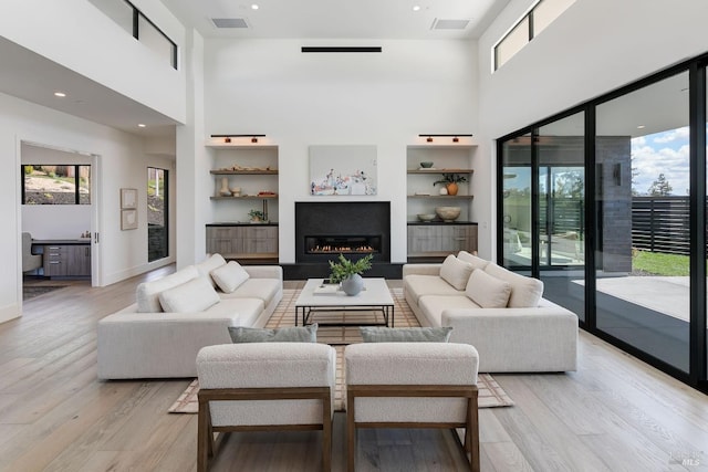 living room featuring built in shelves, a towering ceiling, and light hardwood / wood-style floors