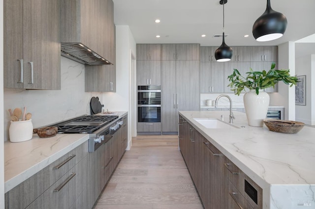 kitchen with light stone counters, sink, light hardwood / wood-style flooring, stainless steel appliances, and decorative light fixtures