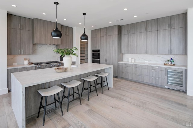 kitchen with a spacious island, beverage cooler, light wood-type flooring, and hanging light fixtures