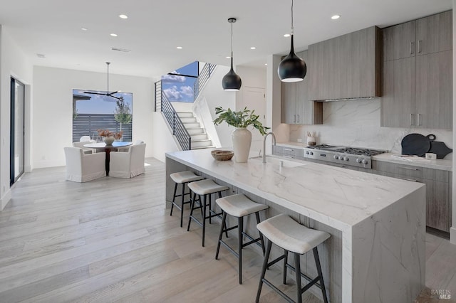 kitchen with light hardwood / wood-style flooring, a center island with sink, hanging light fixtures, and sink