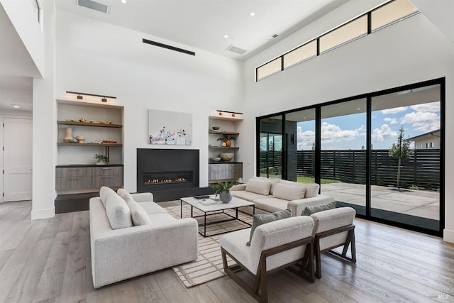 living room with built in shelves, a towering ceiling, and light hardwood / wood-style flooring