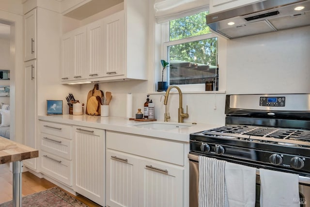 kitchen with light wood-type flooring, gas range, extractor fan, and white cabinets