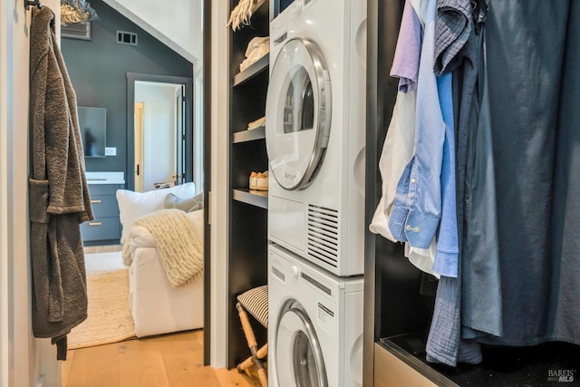 clothes washing area with light hardwood / wood-style floors and stacked washer and clothes dryer