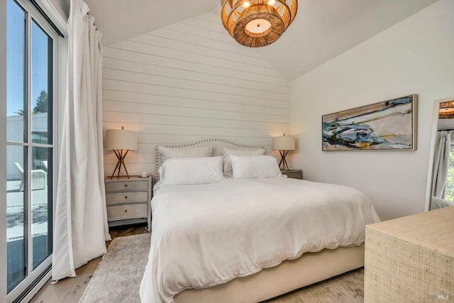 bedroom with lofted ceiling, wood walls, multiple windows, and light hardwood / wood-style flooring