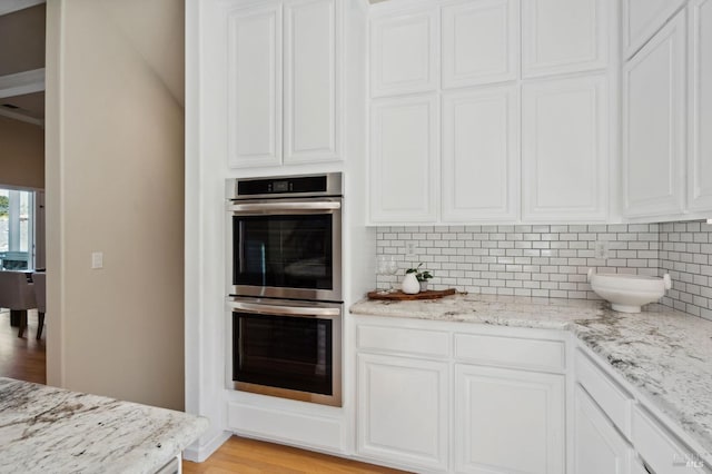 kitchen with light wood-type flooring, white cabinetry, stainless steel double oven, and light stone counters