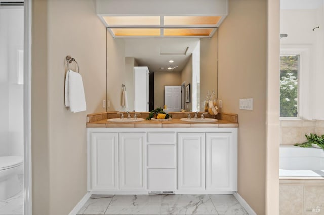 bathroom with tiled bath, vanity, and toilet