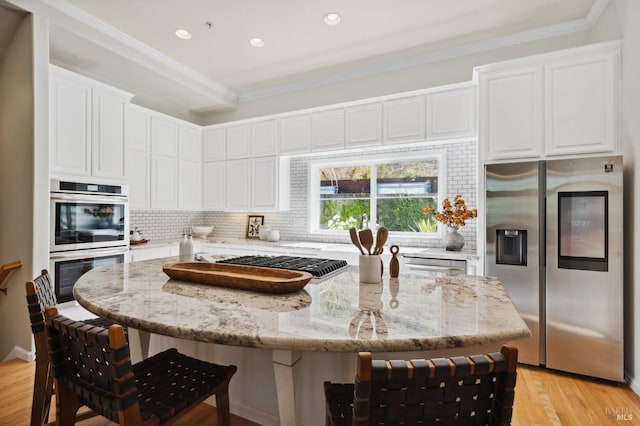 kitchen with light stone countertops, stainless steel appliances, white cabinets, and a center island