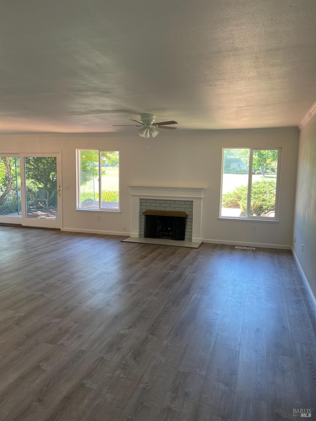 unfurnished living room with a textured ceiling, dark hardwood / wood-style flooring, ceiling fan, and a brick fireplace