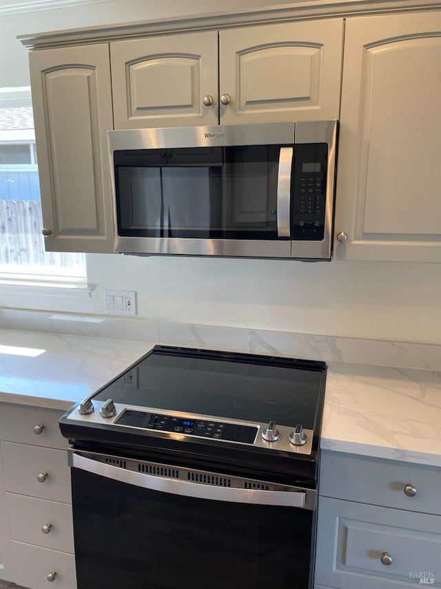 room details with white cabinets, stainless steel microwave, and electric stove