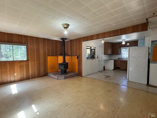 unfurnished living room with wood walls, plenty of natural light, and a wood stove