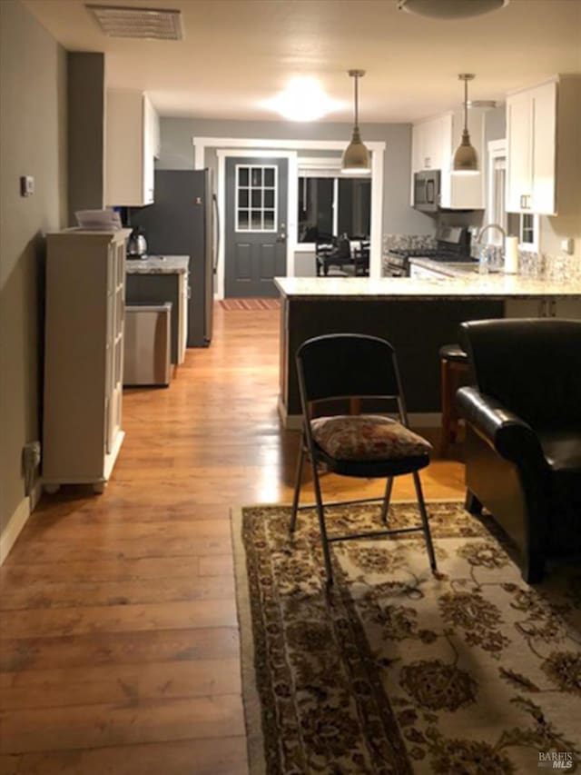 kitchen featuring white cabinets, visible vents, a peninsula, stainless steel appliances, and light wood-type flooring