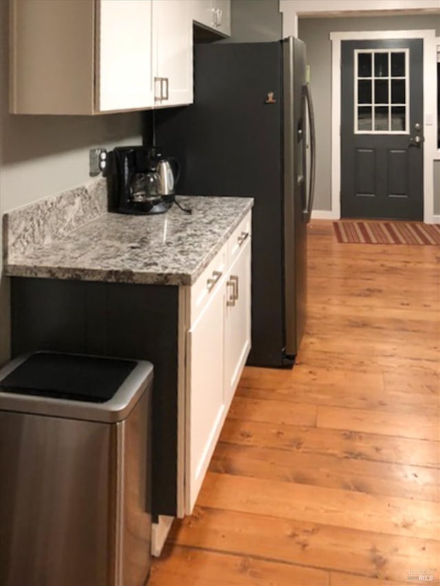 kitchen featuring white cabinetry, light stone countertops, light wood-style floors, and freestanding refrigerator