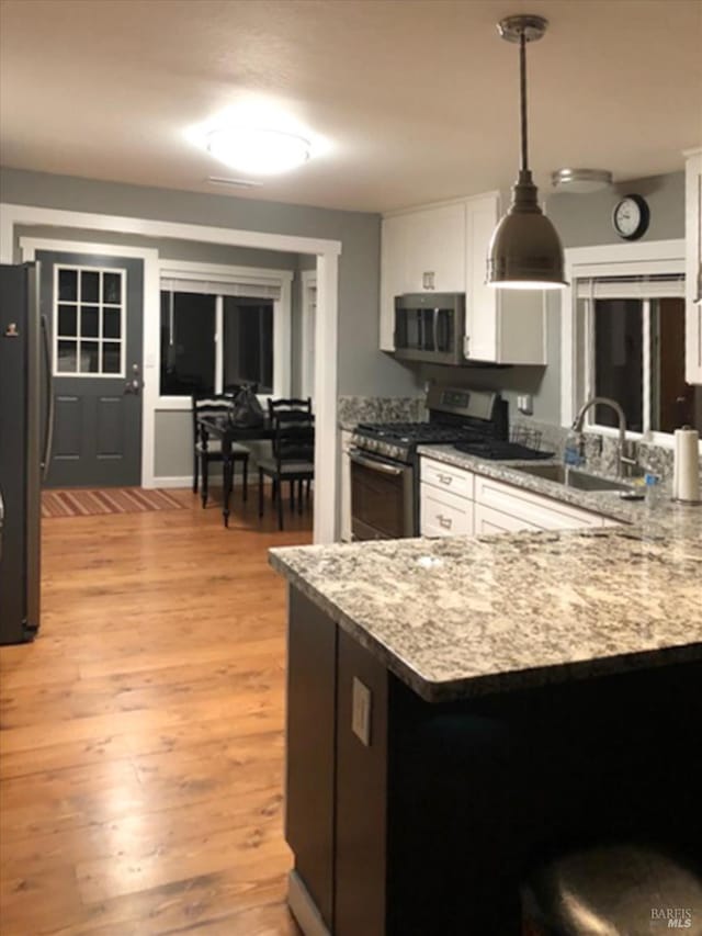 kitchen featuring light wood-style flooring, a peninsula, appliances with stainless steel finishes, white cabinetry, and a sink