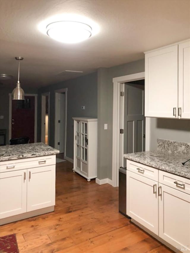 kitchen featuring baseboards, hanging light fixtures, light wood-style floors, white cabinets, and light stone countertops