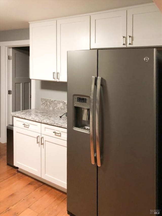 kitchen featuring stainless steel fridge with ice dispenser, white cabinetry, light stone counters, and light wood finished floors