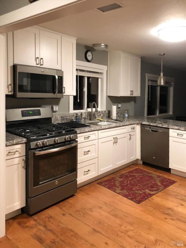 kitchen with white cabinetry, a sink, light wood finished floors, visible vents, and appliances with stainless steel finishes