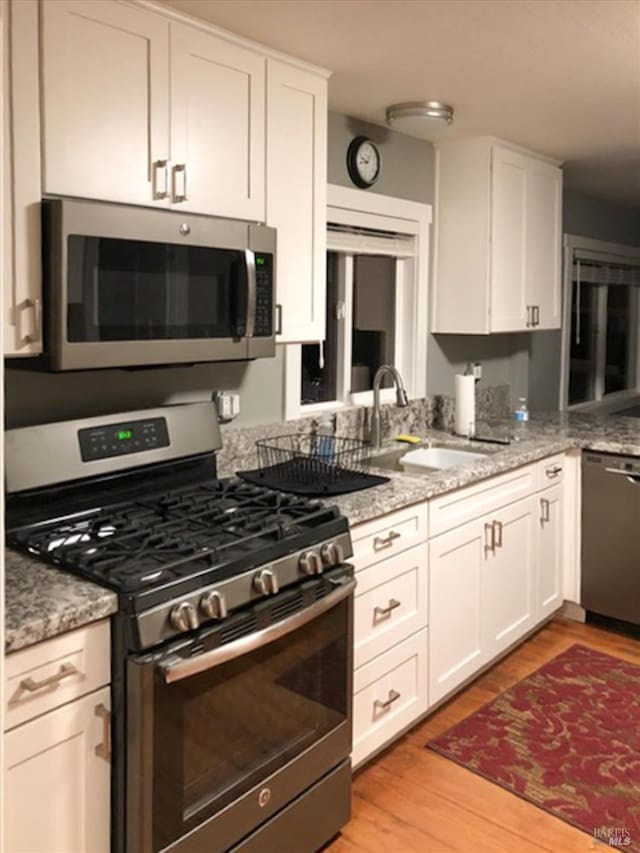kitchen featuring light stone counters, a sink, stainless steel appliances, white cabinets, and light wood-style floors