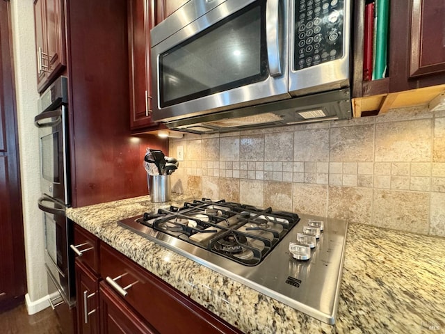 kitchen with appliances with stainless steel finishes, tasteful backsplash, and light stone counters