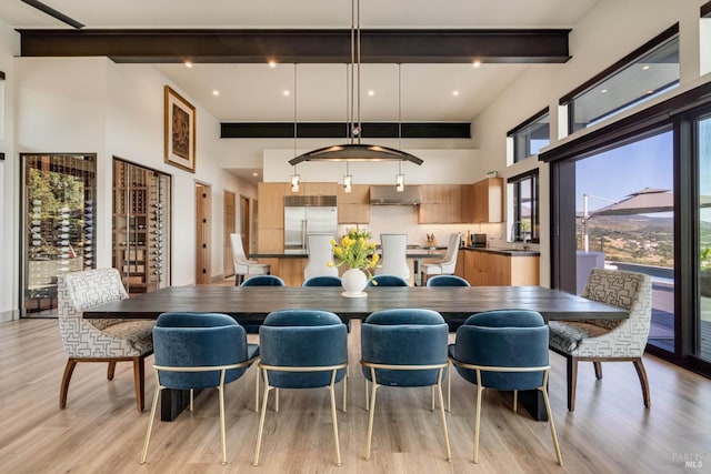 dining room featuring a towering ceiling, beam ceiling, and light wood finished floors