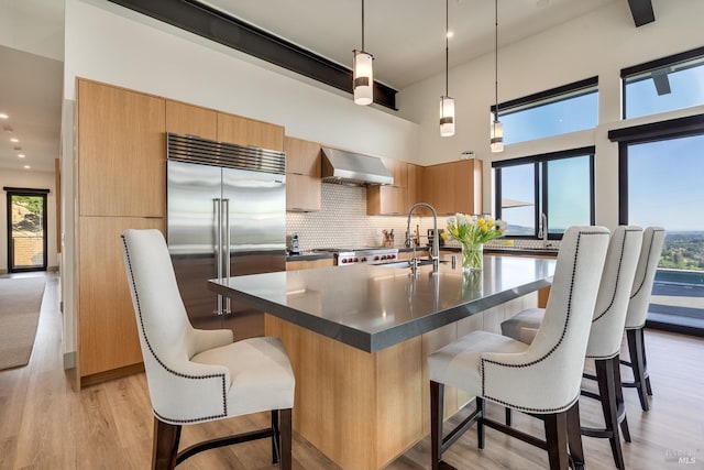 kitchen with modern cabinets, wall chimney exhaust hood, dark countertops, a sink, and stainless steel built in fridge