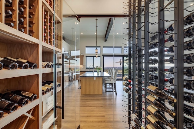 wine room featuring beamed ceiling, light wood-type flooring, a high ceiling, and a sink
