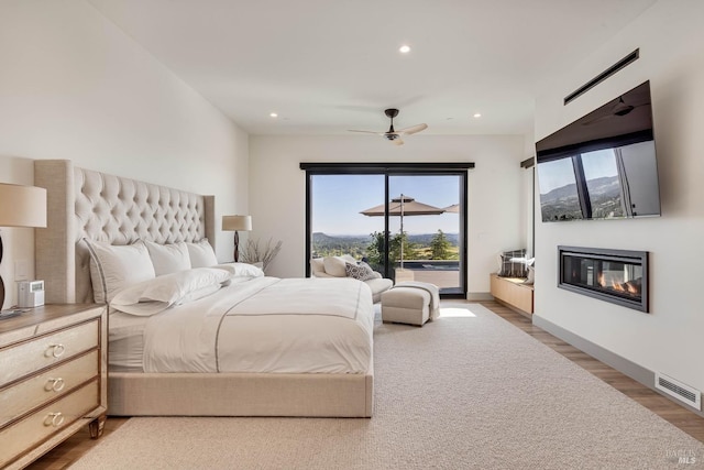 bedroom with access to exterior, light wood finished floors, a glass covered fireplace, visible vents, and recessed lighting