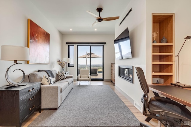 living room featuring visible vents, light wood finished floors, baseboards, ceiling fan, and a glass covered fireplace