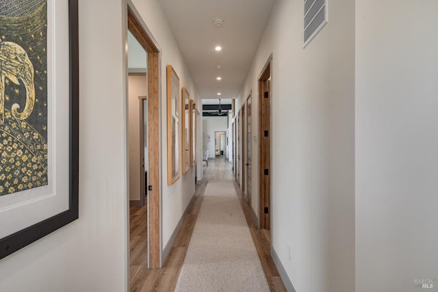 hallway featuring light wood finished floors, baseboards, visible vents, and recessed lighting