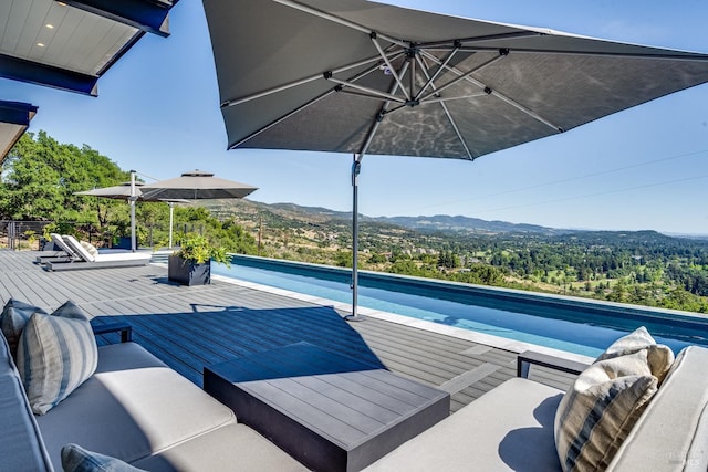 pool featuring a deck with mountain view, an outdoor living space, and a forest view