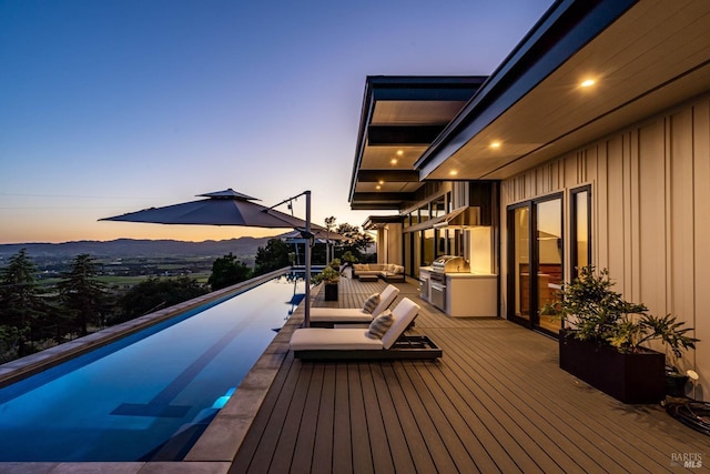 deck at dusk with outdoor lounge area and an infinity pool