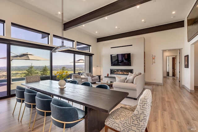 dining area with light wood finished floors, baseboards, recessed lighting, beam ceiling, and a high ceiling