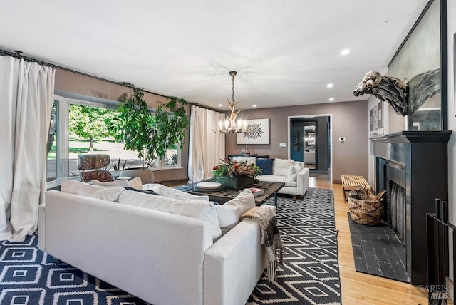 living area featuring recessed lighting, light wood-style floors, a chandelier, and a fireplace with raised hearth