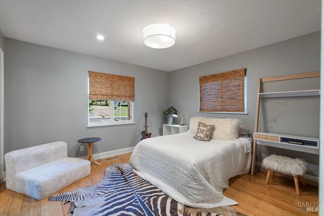 bedroom featuring visible vents, wood finished floors, baseboards, and a textured ceiling