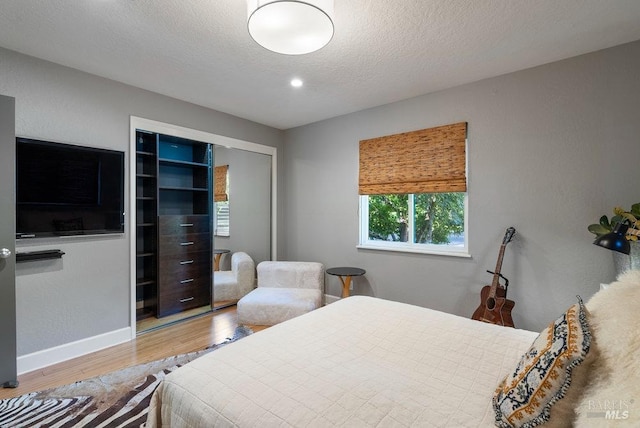 bedroom featuring wood finished floors, baseboards, a closet, and a textured ceiling