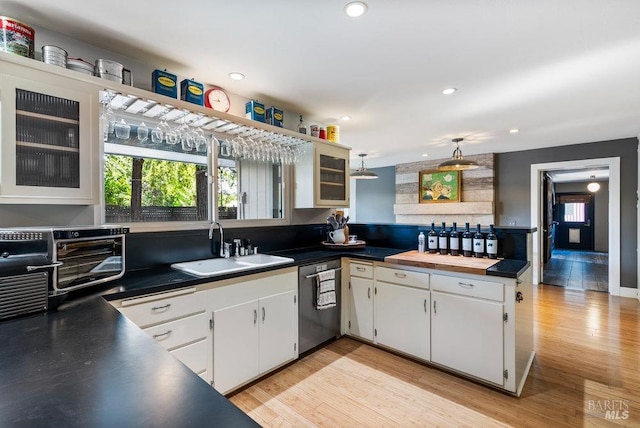 kitchen with a peninsula, a sink, white cabinets, light wood-style floors, and dishwasher