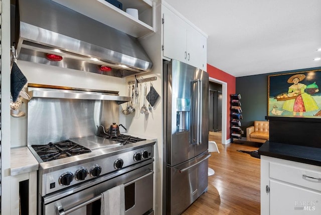 kitchen with stainless steel appliances, white cabinets, light wood-style floors, wall chimney range hood, and tasteful backsplash