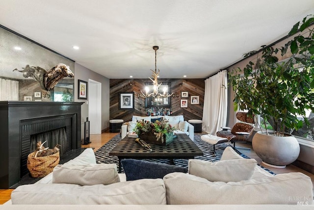 living room with an accent wall, wood walls, recessed lighting, a fireplace, and an inviting chandelier