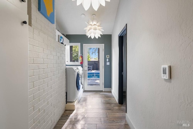 washroom with wood finished floors, separate washer and dryer, brick wall, baseboards, and a textured wall