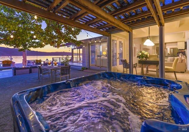 pool at dusk featuring a hot tub, a pergola, a water view, and a patio area