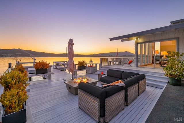 deck at dusk featuring a water and mountain view and an outdoor living space with a fire pit