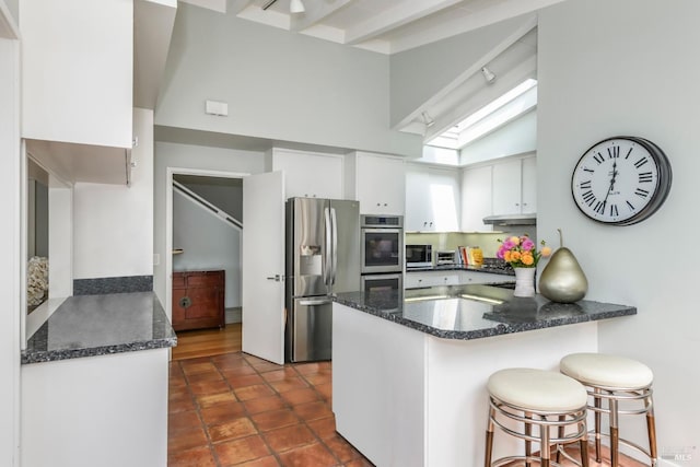 kitchen featuring kitchen peninsula, beamed ceiling, stainless steel appliances, and white cabinets