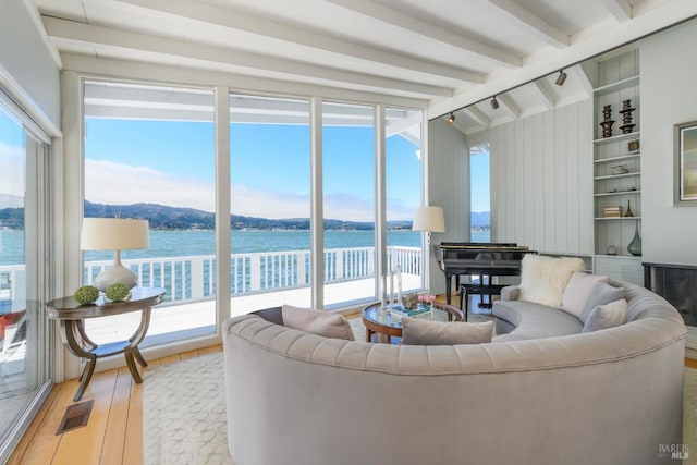 living room featuring lofted ceiling with beams, built in shelves, a water view, and light hardwood / wood-style floors