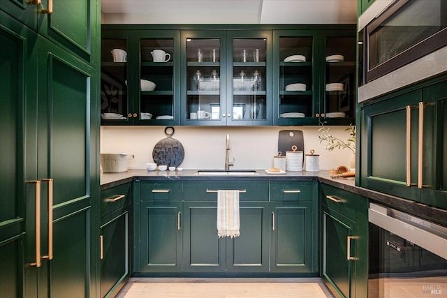 bar with light wood-type flooring, green cabinetry, and sink