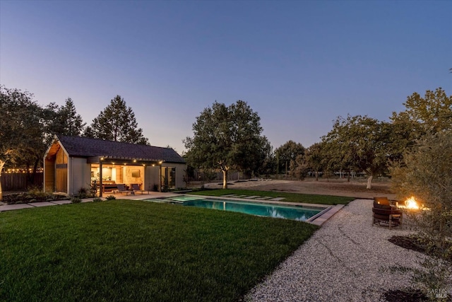 pool at dusk with a yard, a patio area, and an outbuilding