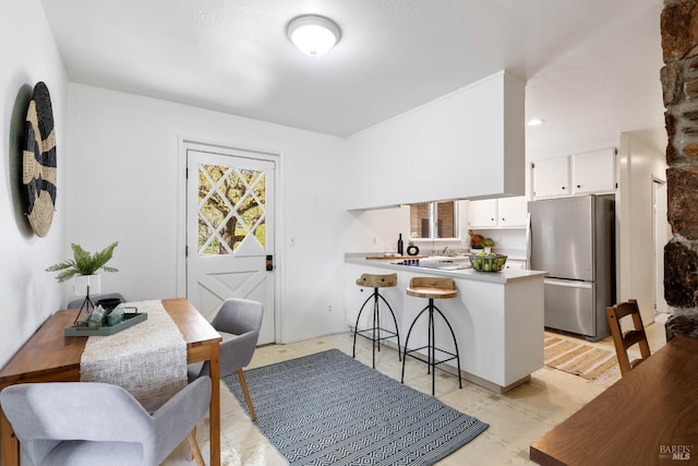 kitchen featuring kitchen peninsula, a breakfast bar, white cabinetry, and stainless steel refrigerator