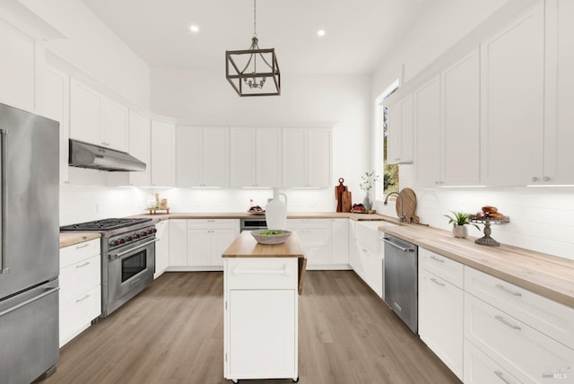 kitchen with wood counters, a kitchen island, under cabinet range hood, stainless steel appliances, and a sink