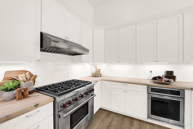 kitchen with tasteful backsplash, white cabinetry, butcher block counters, under cabinet range hood, and stainless steel appliances