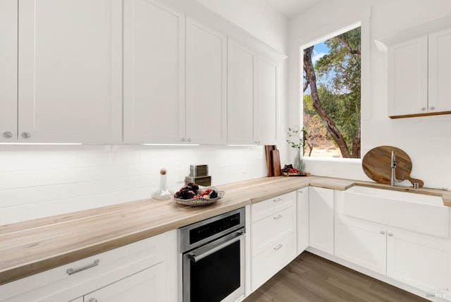 kitchen with white cabinets, oven, dark wood-style floors, wood counters, and backsplash